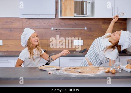 portrait de la joyeuse femme et de son enfant fille portant un tablier aiment passer du temps ensemble dans la cuisine, la cuisson et la cuisine ensemble, jouer ou danser en kitch Banque D'Images