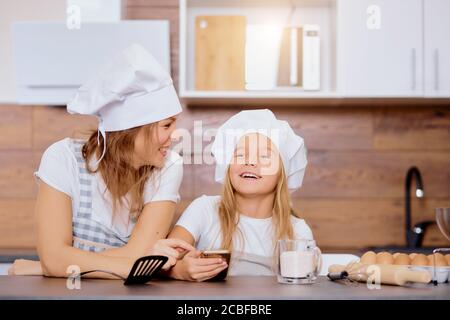 portrait d'une femme avec une petite fille pensant à cuire quelque chose dans la cuisine, portant des tabliers et des casquettes pour la cuisine Banque D'Images