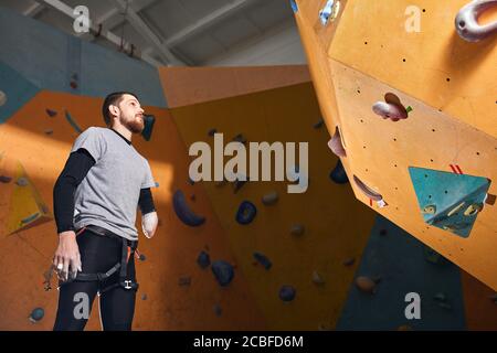 La vue en angle bas de l'homme sportif avec handicap physique, debout et regardant le mur d'escalade artificiel, est venu à des cours d'entraînement d'escalade, rêve à Banque D'Images