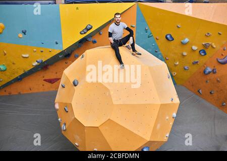 Un jeune homme d'affaires réussi avec un handicap physique assis au sommet d'un mur en pierre de forme ronde dans la salle de gym de bloc, heureux et heureux, a souligné Banque D'Images