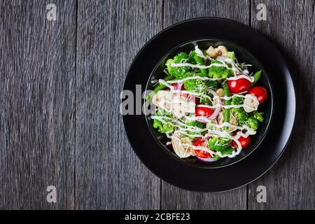 salade de fleurons de brocoli, haricots verts cuits à la vapeur, champignons, tomates nappées de parmesan râpé et sauce au yaourt dans un bol noir, chapeau de terre Banque D'Images