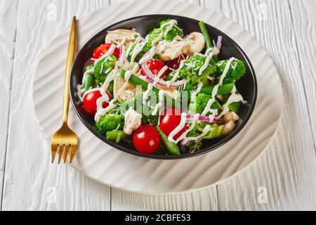 salade de fleurons de brocoli, haricots verts cuits à la vapeur, champignons, tomates oignons rouges nappés de parmesan râpé et sauce au yaourt dans un arc noir Banque D'Images