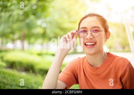 Femme asiatique portant des lunettes sourire heureux avec la nature verte à l'extérieur arrière-plan Banque D'Images