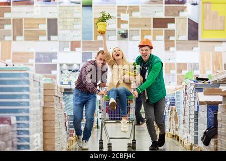 un jeune couple caucasien marié aime faire du shopping ensemble, une femme à bord d'un chariot dans l'hypermarché, mari et employé d'entrepôt tiennent le chariot ensemble, hap Banque D'Images