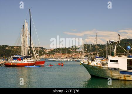 Vue panoramique sur le port avec des bateaux amarrés, un groupe de personnes en kayak et la ville côtière en arrière-plan en été, Lerici, la Spezia, Italie Banque D'Images