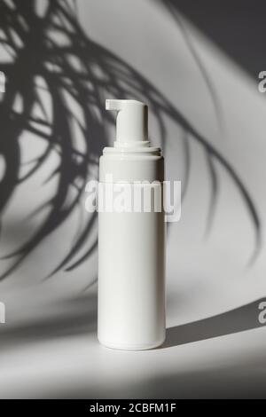 Maquette de bouteille en plastique blanc avec pompe. Distributeur de savon, gel intime, shampooing, gel douche design d'emballage sur fond blanc avec ombre de plante Banque D'Images