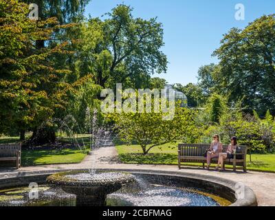 Deux jeunes femmes assises près de la piscine avec fontaine, University of Oxford Botanical Gardens, Oxford, Oxfordshire, Angleterre, Royaume-Uni, GB. Banque D'Images