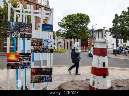 North Berwick, East Lothian, Écosse, Royaume-Uni, 13 août 2020. Effets Covid-19 : une exposition de photos de la précédente Fringe-by-the-Sea rappelle aux visiteurs l'annulation du festival de cette année qui aurait été en ce moment alors qu'une femme plus âgée portant un masque facial se promène devant Banque D'Images