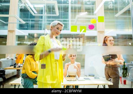 femme élégante et élégante en costume jaune derrière un mur de verre. copy space.leader de l'équipe planifiant leur journée de travail Banque D'Images