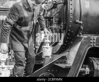 Vue monochrome d'un membre de l'équipe de locomotive à vapeur qui change les phares d'une locomotive à moteur à vapeur du Royaume-Uni. Banque D'Images