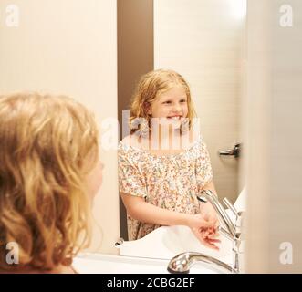 Une petite fille lave ses mains dans une caravane. Elle regarde dans un miroir. Banque D'Images