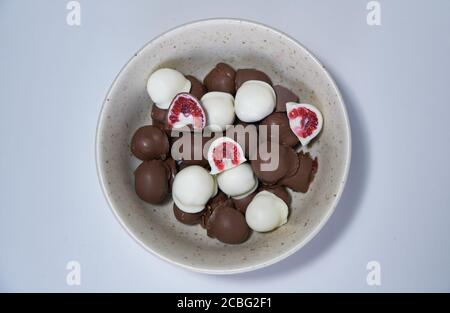 la main de femme choisit et attrapant rouge frais et brillant frais framboises enrobées de chocolat noir et blanc fait maison Banque D'Images