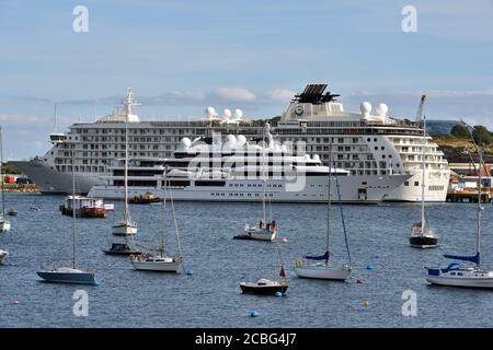 Le luxueux super yacht Katara, propriété de la famille royale du Qatar, passe devant le bateau de croisière de luxe le monde amarré au port de Falmouth. Banque D'Images