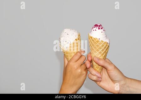 Les mains de la mère et de la fille maintiennent le maïs glacé avec de la crème glacée au lait. Isolé sur un fond gris. Banque D'Images