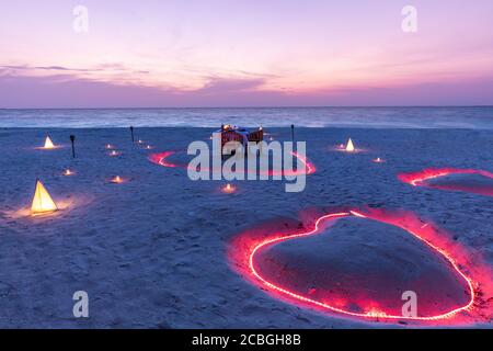 Un jeune couple partage un dîner romantique avec des bougies coeur sur la plage de sable de mer. Dîner romantique au coucher du soleil avec coeur de bougies sur la plage de sable de mer Banque D'Images
