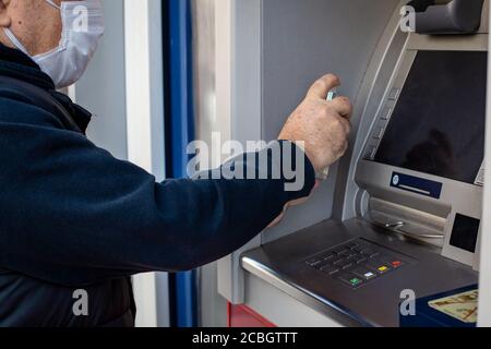 Un homme désinfecte l'écran et le clavier du distributeur de billets avant de retirer de l'argent. Banque D'Images