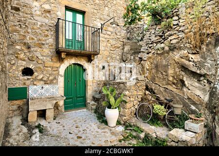 Maison en pierre d'architecture traditionnelle de Sicile dans la vieille rue du village de Mistretta : porte, balcon, lavoir, pot avec barbarie et vélo Banque D'Images