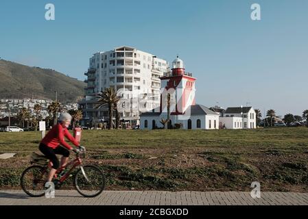 Femme âgée à vélo à la promenade de Sea point au Cap avec le phare de Green point en arrière-plan-Motion flou sur le cycliste. Banque D'Images