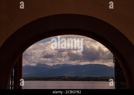 Une image artistique abstraite de coucher de soleil d'une vue sur le lac Léman, Suisse à travers une fenêtre voûtée. Il y a des maisons, des montagnes alpines, des fermes Banque D'Images