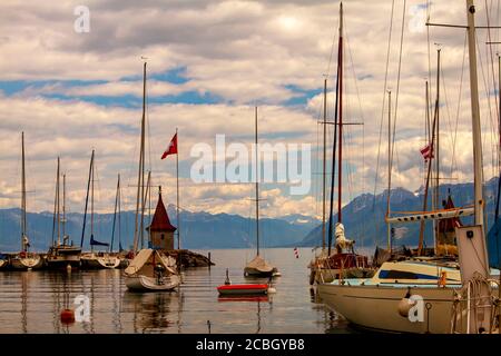 Vue sur le paysage de la marina sur la côte du lac Léman, en Suisse. Eaux claires du lac, un phare d'époque, un quai, une jetée, des voiles et un suisse Banque D'Images