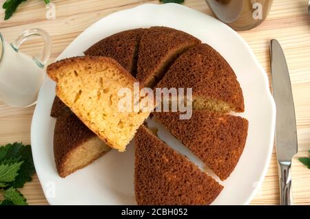 Tranché, divisé tarte éponge en portionsand une tasse de café avec du lait sur un fond en bois. Une pièce est prise et posée sur le dessus. Minimaliste. Banque D'Images