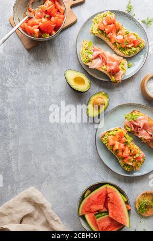 Pain maison avec tartiner à l'avocat, tomates hachées et herbes. Avec jambon de Parme. Concept de petit déjeuner sain vu d'en haut. Avec espace de copie Banque D'Images