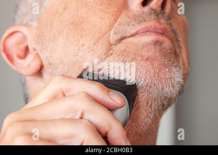 Homme âgé avec barbe de 3 jours non taillée avec tondeuse ou rasoir électrique. Banque D'Images