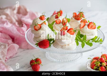 Mini Pavlova meringue niche avec de la crème fouettée et des fraises fraîches bio maison. Les mini desserts meringue sont présentés sur un gâteau en verre Banque D'Images