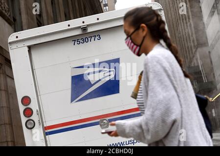 New York, États-Unis. 12 août 2020. Une femme traverse la rue en passant devant un camion du United State postal Service stationné le long de la 45e rue à Manhattan, New York, NY, le 12 août 2020. Le président Donald Trump a annoncé qu'il s'opposait au financement du service postal des États-Unis de peur qu'il ne soit utilisé pour le vote par courrier et qu'il nuirait à sa réélection. (Anthony Behar/Sipa USA) crédit: SIPA USA/Alay Live News Banque D'Images