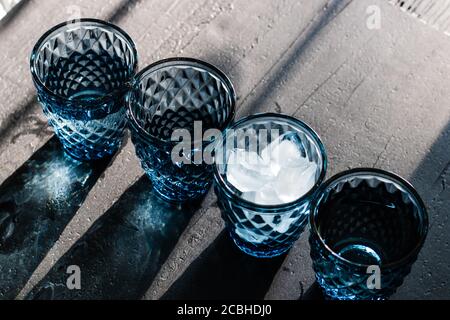 Verres en cristal bleu à motifs géométriques avec glace et boissons en diagonale et en donnant des ombres colorées sur le dessus noir Banque D'Images