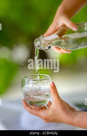 Verser de l'eau. Gros plan versant de l'eau fraîche purifiée de la bouteille sur une table sur un fond flou naturel Banque D'Images