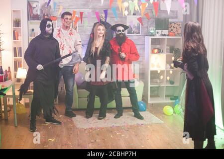 Vue arrière de la sorcière prenant des photos de zombie et de ses amis lors de la fête d'halloween. Banque D'Images