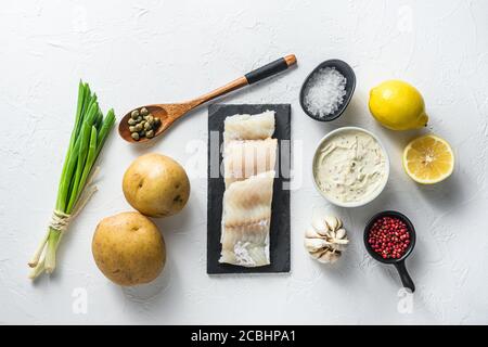 Les ingrédients traditionnels du poisson et des chips recettes de filets de morue crus sur la pâte d'ardoise de pierre, le potatoe, la sauce tartare, le citron, les câpres, les herbes vertes de l'ail, le sel Banque D'Images