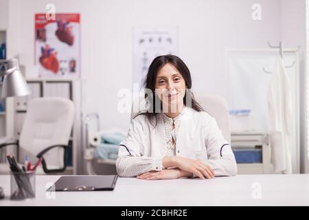 Portrait d'une femme réussie médecin dans le bureau de l'hôpital portant un manteau blanc regardant l'appareil photo. Joyeux medic spécialiste. Banque D'Images