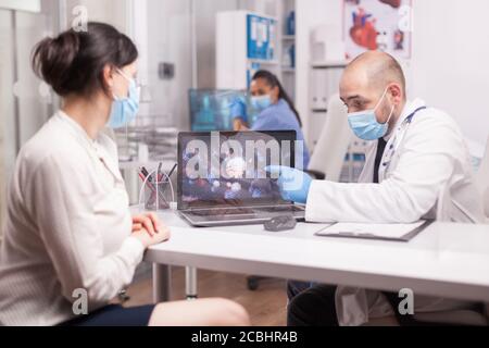 Médecin expliquant les symptômes du covid 19 à une jeune patiente dans le bureau de l'hôpital pendant l'examen. Banque D'Images