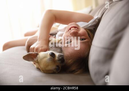 Rire fille allongé avec son chien sur le canapé regardant à l'appareil photo Banque D'Images