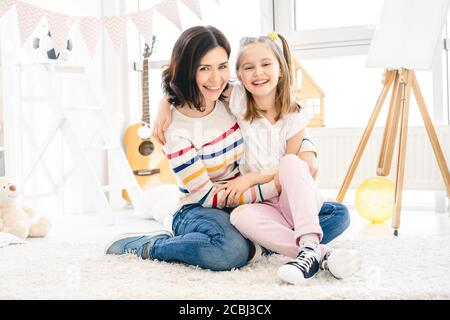 Femme souriante avec une petite fille assise sur le sol à la maison Banque D'Images