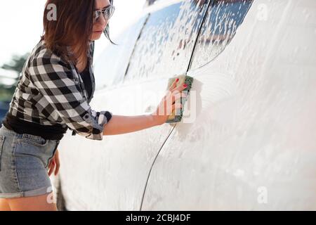 Main de fille avec éponge de nettoyage de voiture en utilisant la mousse sur la voiture laver Banque D'Images