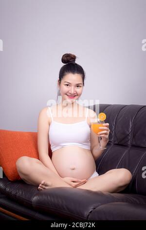 Femme enceinte mangeant des aliments avec un ingrédient pour un concept sain : jeune femme enceinte asiatique tient du jus d'orange frais dans le verre avec le visage souriant Banque D'Images