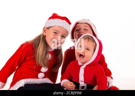 3 enfants, 2 garçons (1 an - 4 ans) 1 fille (6 ans) assise ensemble sur le sol en costume du Père Noël riant. Isolé sur blanc Banque D'Images