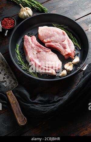 Rôti de porc cru dans une poêle sur un table de cuisine rustique en bois avec des ingrédients de poivre de romarin à l'ail côté du couteau de la grille et du butter Banque D'Images