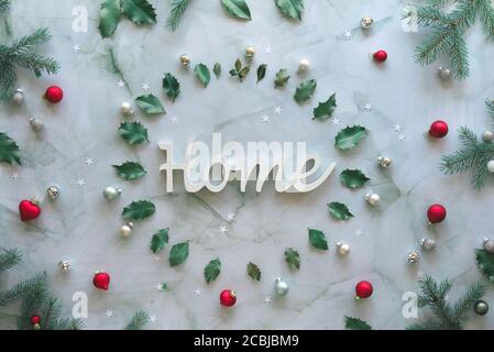 Appartement de Noël en gris, vert, argent et rouge. Mot Home dans un cercle de marbre. Arrière-plan de Noël avec brindilles de sapin naturel, feuilles de houx et boules de verre. Banque D'Images