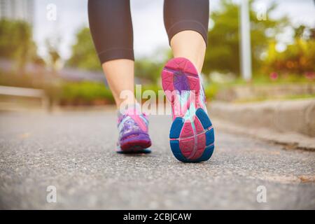 Gros plan sur la chaussure, les pieds d'athlète de coureur courir sur la route sous la lumière du soleil le matin. Banque D'Images