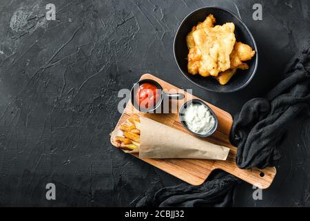 Fish and chips dans un cône de papier sur la trempette de planche à découper et citron - morue frite, frites, tranches de citron, sauce tartare, tomatoe de ketchup et mushy Banque D'Images