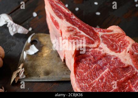 Bœuf cru Dallas steak, qui se trouve sur le couteau de coupe. Viande de bœuf crue préparée pour la cuisson des steaks. À côté des ingrédients pour cuisiner des steaks, des épices Banque D'Images