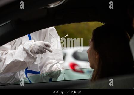 14 août 2020, Bade-Wurtemberg, Neuenburg am Rhein: Un employé de DRK en costume de protection se tient à la fenêtre ouverte d'une voiture pendant qu'il effectue le test de corona dans un parking d'autoroute. Après leur retour de vacances, les voyageurs peuvent se faire tester pour le nouveau virus corona dans le parking de Neuchâtel-est. Photo: Philipp von Ditfurth/dpa Banque D'Images