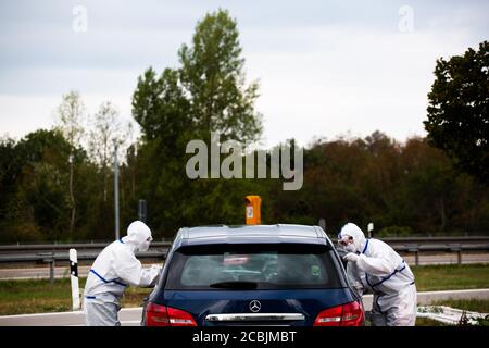 14 août 2020, Bade-Wurtemberg, Neuenburg am Rhein: Deux employés du DRK sont debout dans une combinaison de protection à la fenêtre ouverte d'une voiture pendant qu'ils effectuent l'essai de frottis pour l'essai de corona dans un parking d'autoroute. Après leur retour de vacances, les voyageurs peuvent se faire tester pour le nouveau virus corona dans le parking de Neuchâtel-est. Photo: Philipp von Ditfurth/dpa Banque D'Images