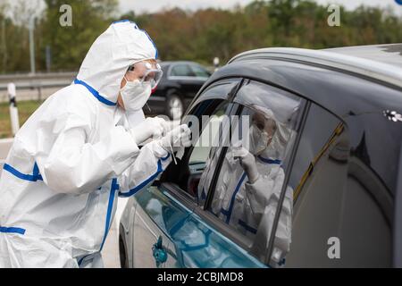 14 août 2020, Bade-Wurtemberg, Neuenburg am Rhein: Un employé de DRK en costume de protection se tient à la fenêtre ouverte d'une voiture pendant qu'il effectue le test de corona dans un parking d'autoroute. Après leur retour de vacances, les voyageurs peuvent se faire tester pour le nouveau virus corona dans le parking de Neuchâtel-est. Photo: Philipp von Ditfurth/dpa Banque D'Images