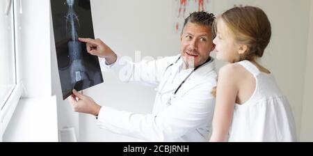 Le docteur en manteau blanc examine le dos de la fille et montre une radiographie Banque D'Images