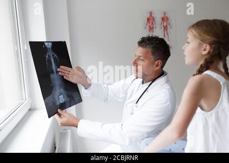 Le docteur en manteau blanc examine le dos de la fille et montre une radiographie Banque D'Images